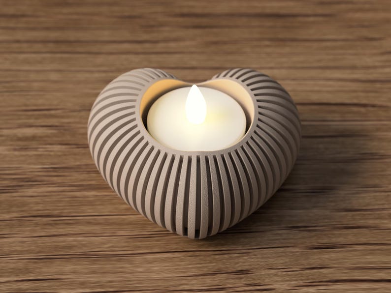 May include: A heart-shaped candle holder with a lit candle inside. The holder is light gray with vertical grooves, and the candle emits a warm, inviting glow. The holder sits on a wooden surface.