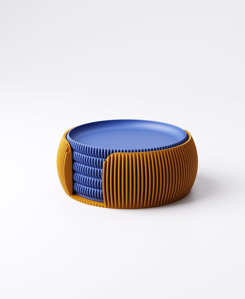 May include: A stack of blue plates inside a mustard yellow holder. The holder has a ribbed design. The plates are stacked neatly, with the top plate visible. The holder is a rounded shape, with vertical lines. The background is white.