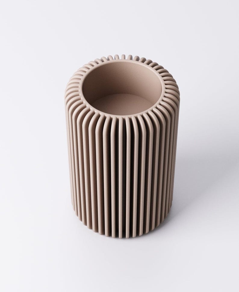 May include: A cylindrical, beige-colored vase with vertical ribbed detailing. The top rim has a rounded, textured edge. The interior is a smooth, open space. The vase is a neutral tone, suitable for various decor styles.