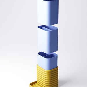 May include: A modular, three-part container in shades of blue and yellow. The top section is a light blue lid. The middle sections are light blue containers. The base is a yellow, ribbed structure with a small tray. The design is modern and minimalist.