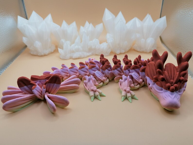 May include: An assortment of fantasy-themed sculptures in shades of white, pink, and brown. The collection includes crystal formations and a stylized dragon with a detailed head and body. The pieces are arranged on a light-colored surface.