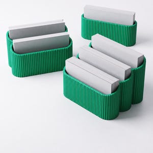May include: Several green, ribbed card holders filled with stacks of white cards are arranged on a white surface. The holders have a unique, curved design, and the cards appear to be blank.