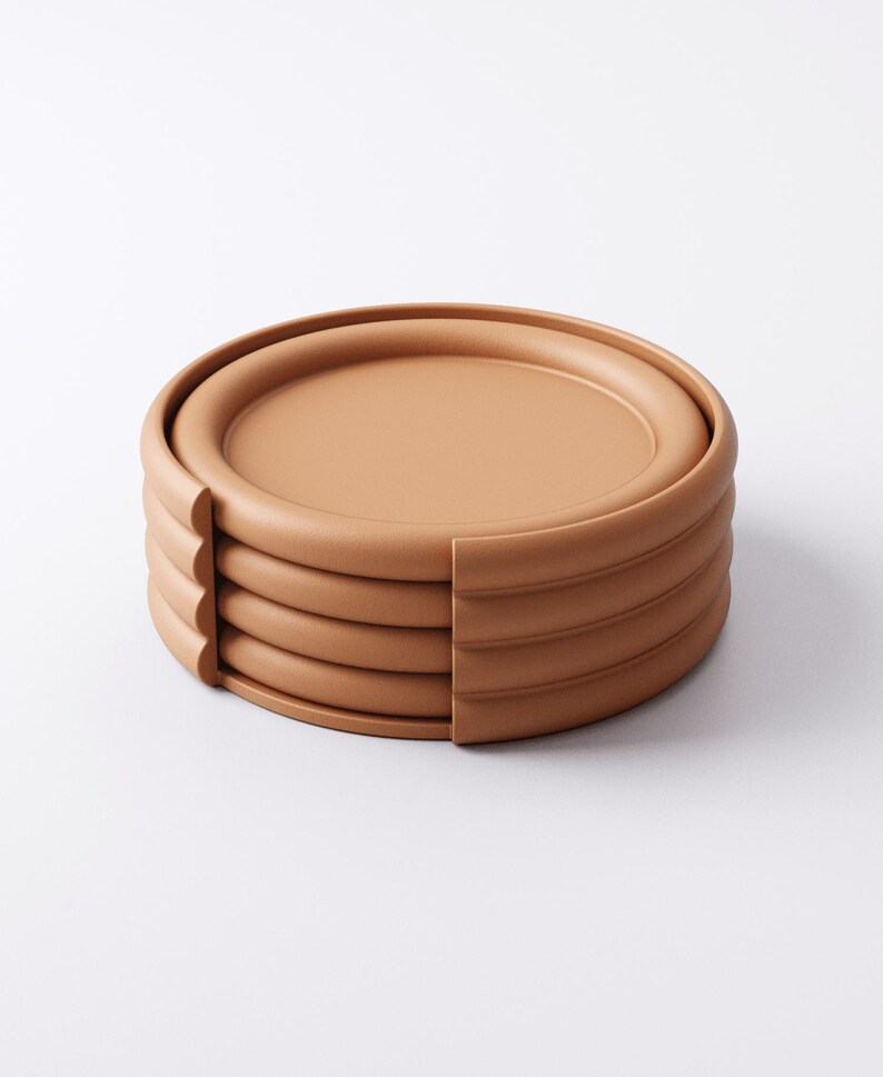 Puede incluir: Una pila de cinco posavasos redondos de color terracota. Cada posavasos tiene un borde elevado y un centro plano. La pila est&aacute; parcialmente cortada por un lado, revelando la construcci&oacute;n en capas. Los posavasos est&aacute;n dise&ntilde;ados para proteger las superficies de las marcas de bebidas.
