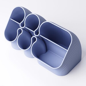 May include: A modern, blue desk organizer with a unique, curved design. The organizer features multiple compartments of varying sizes, separated by white dividers. The exterior has a ribbed texture, and the interior is a lighter shade of blue.