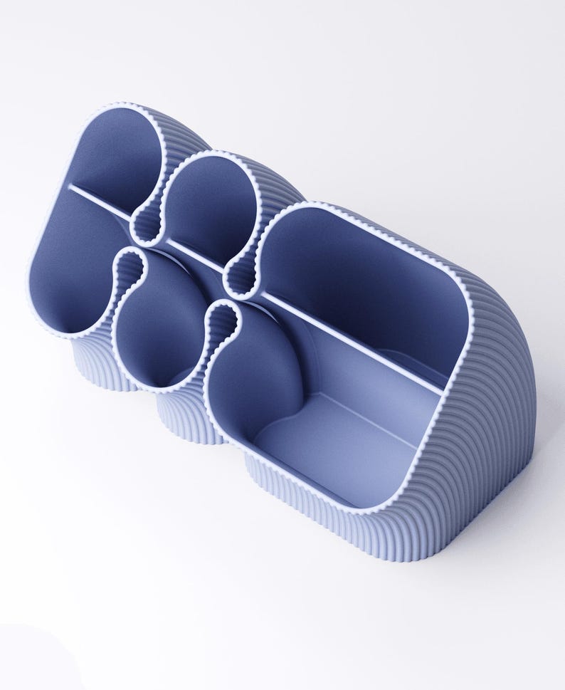 May include: A modern, blue desk organizer with a unique, curved design. The organizer features multiple compartments of varying sizes, separated by white dividers. The exterior has a ribbed texture, and the interior is a lighter shade of blue.