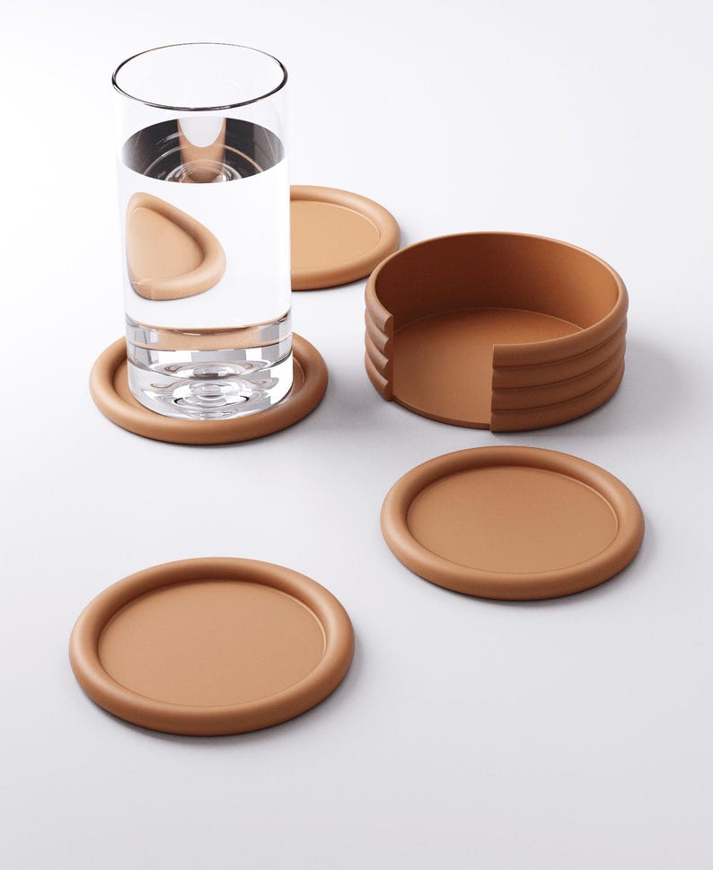 Puede incluir: Un juego de posavasos marrones con un soporte a juego. Un posavasos est&aacute; debajo de un vaso de agua. Los posavasos son redondos con un borde elevado. El soporte es un recipiente marr&oacute;n semicircular con un dise&ntilde;o acanalado.