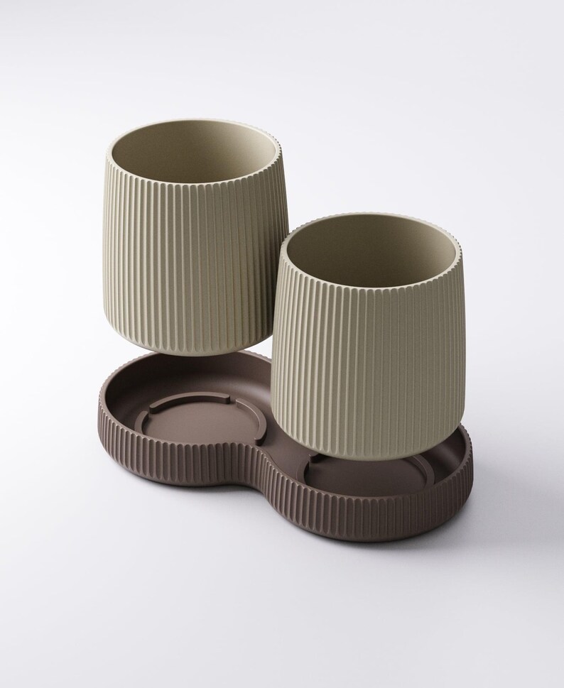 May include: Two beige ribbed ceramic tumblers sit above a brown, double-sectioned tray. The tumblers have a cylindrical shape with vertical grooves. The tray has a similar ribbed design around its edges, creating a cohesive set.