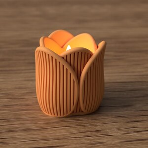 May include: A candle holder shaped like a tulip flower, with a warm orange glow emanating from within. The holder is a light orange color with vertical lines, and sits on a wooden surface.