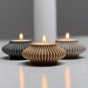 Puede incluir: Tres candelabros de madera con velas encendidas. Los portavelas son en tonos grises y madera natural, con un dise&ntilde;o acanalado. Las llamas son brillantes sobre el fondo suave. Un acento decorativo para el hogar.