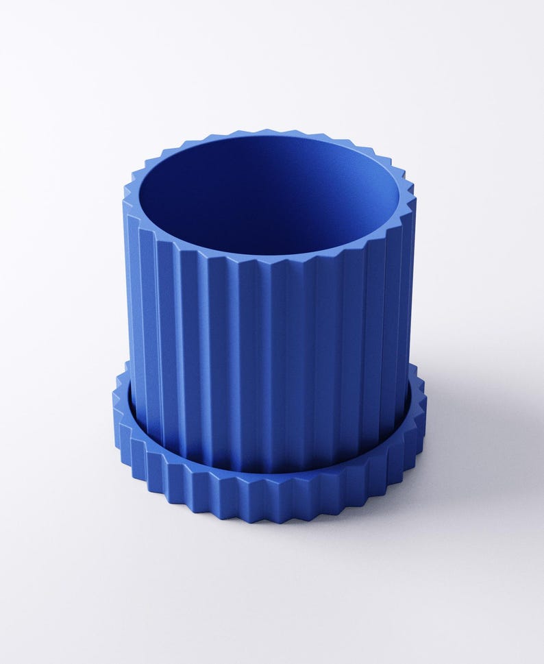 May include: A cobalt blue cylindrical planter with a matching saucer. The planter has vertical, ridged detailing around the exterior and a zig-zag pattern on the rim and saucer edge. The planter is designed to hold plants.