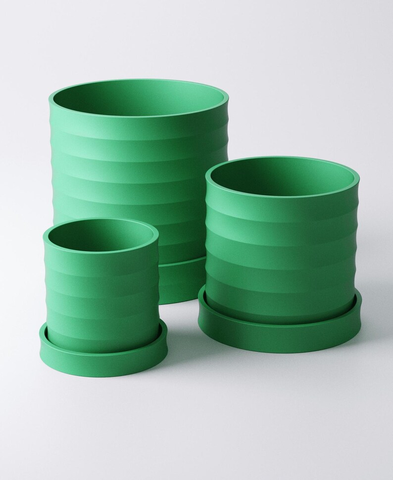 Op de afbeelding: Drie groene cilindrische bloempotten van verschillende maten. Elke pot heeft een geribbeld ontwerp en staat op een bijpassende ronde basis. De potten zijn felgroen van kleur en staan tegen een witte achtergrond.