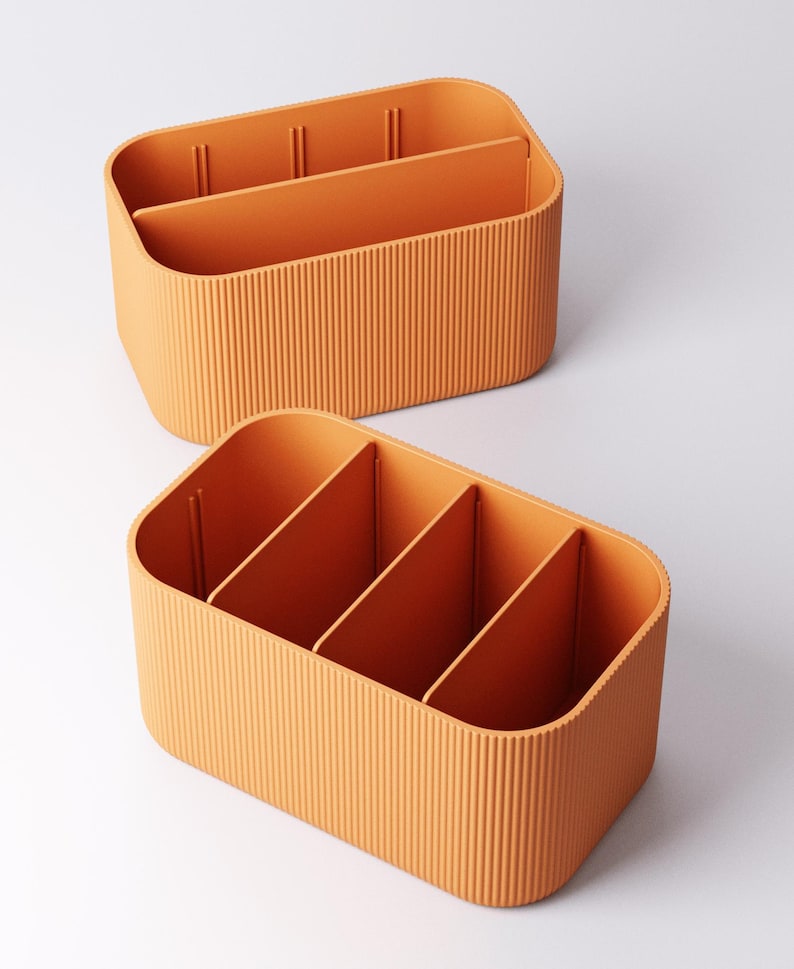 May include: Two orange storage organisers with vertical ribbed sides and internal dividers. The organisers have rounded corners and are designed to hold various items. The dividers create multiple compartments for organisation. The colour is a warm, inviting orange.