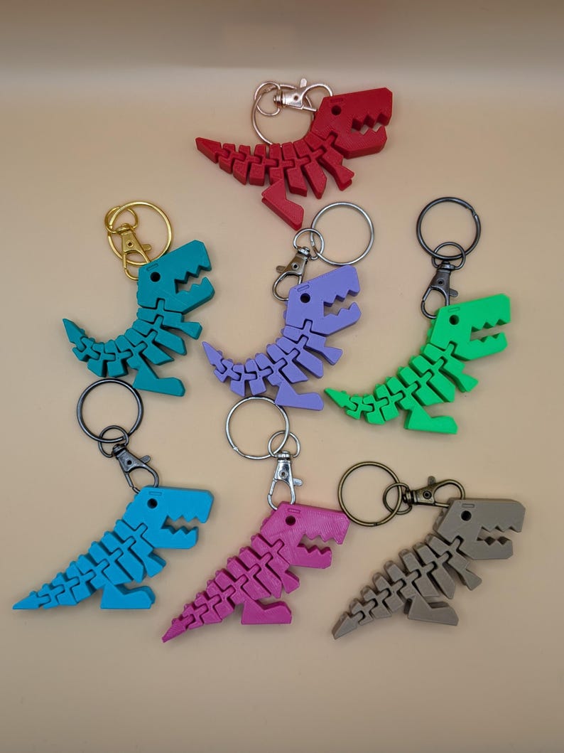 May include: A collection of colorful dinosaur keychains in red, teal, purple, green, blue, pink, and gray. Each keychain features a segmented dinosaur design with a metal keyring and clasp.