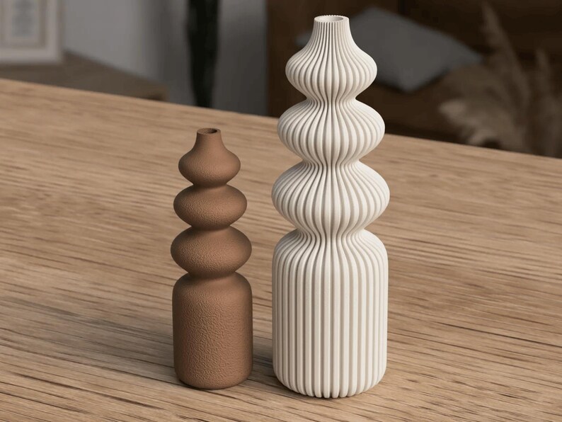 May include: Two decorative vases. One is a tall, white, ribbed vase with a bulbous shape. The other is a smaller, brown vase with a similar shape. Both vases are on a wooden surface.