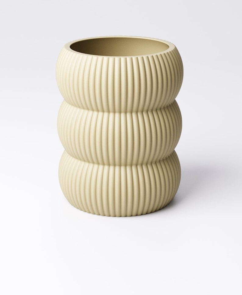 May include: A light beige, ribbed ceramic vase with a stacked, rounded design. The vase has a wide opening and a textured, vertical groove pattern. The neutral color and unique shape make it a decorative home accent.