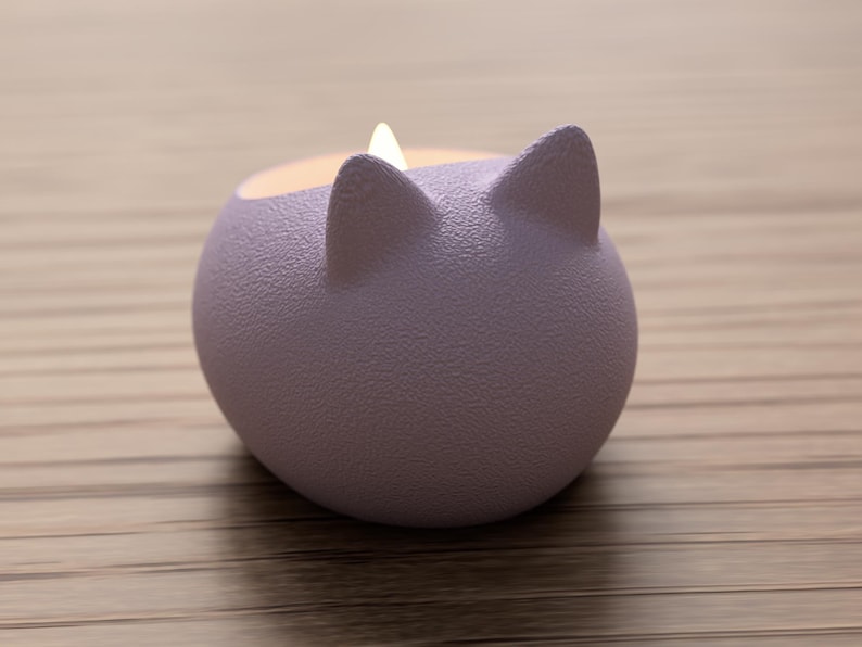 May include: A lavender-colored, cat-shaped candle holder with two pointed ears. The candle holder has a textured surface and contains a lit candle. The background is a light brown wooden surface.