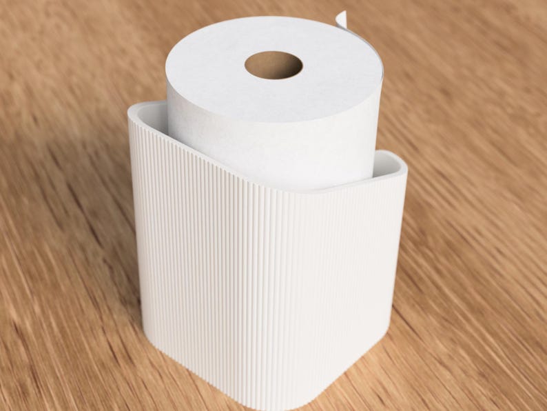 Op de afbeelding: Een witte toiletpapierrol in een bijpassende houder. De houder heeft een gebogen ontwerp met verticale lijnen. De achtergrond is een lichtbruin houten oppervlak. De toiletpapierrol is wit.