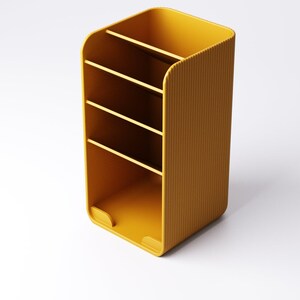 May include: Mustard yellow desk organizer with four compartments. The organizer has a ribbed texture on the sides and a rounded top. The bottom has two small cutouts. The organizer is designed to hold pens, pencils, and other office supplies.
