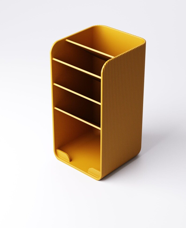 May include: Mustard yellow desk organizer with four compartments. The organizer has a ribbed texture on the sides and a rounded top. The bottom has two small cutouts. The organizer is designed to hold pens, pencils, and other office supplies.