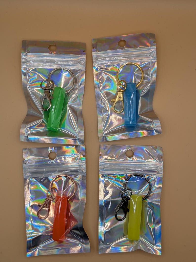 May include: Four keychains in iridescent pouches. Each keychain has a different colored holder: green, blue, orange, and yellow-green. The keychains have a metal ring and a clasp. The pouches are sealed and have a small hole at the top.