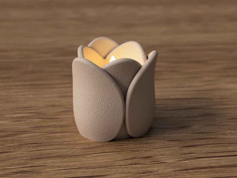May include: A beige tulip-shaped candle holder with a lit candle inside. The holder has a textured surface and is sitting on a wooden surface. The candle holder is designed to resemble a tulip flower.