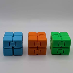 May include: Three colorful fidget cubes in blue, orange, and green. Each cube is composed of eight smaller cubes connected by hinges, allowing for flexible movement and manipulation. The cubes are arranged in a row against a white background.