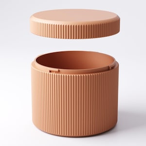 May include: A peach-colored, cylindrical container with a matching lid. The lid is slightly elevated, revealing the interior of the container. Both the lid and the container have vertical, ridged detailing, creating a textured appearance. The container is designed to store items.