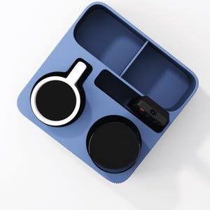 May include: A light blue rectangular organizer tray with rounded corners and a textured outer edge. The tray features multiple compartments containing a white and black mug, a black cup, and a small black electronic remote control device.