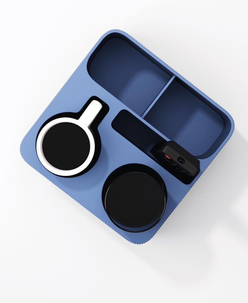 May include: A light blue rectangular organizer tray with rounded corners and a textured outer edge. The tray features multiple compartments containing a white and black mug, a black cup, and a small black electronic remote control device.