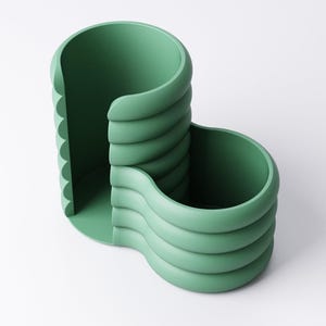 May include: A sage green desk organizer with a unique, layered design. The organizer features two open compartments and a scalloped edge, perfect for storing pens, pencils, and other office supplies. The smooth, matte finish adds a modern touch.