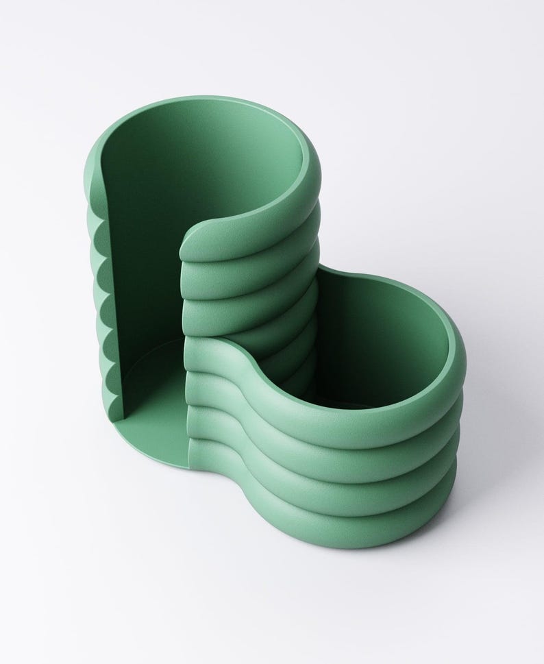 May include: A sage green desk organizer with a unique, layered design. The organizer features two open compartments and a scalloped edge, perfect for storing pens, pencils, and other office supplies. The smooth, matte finish adds a modern touch.