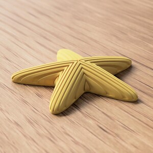 May include: A yellow starfish-shaped object with textured ridges, resting on a wooden surface. The starfish has five points and a slightly curved shape. The wooden surface has a natural wood grain pattern.