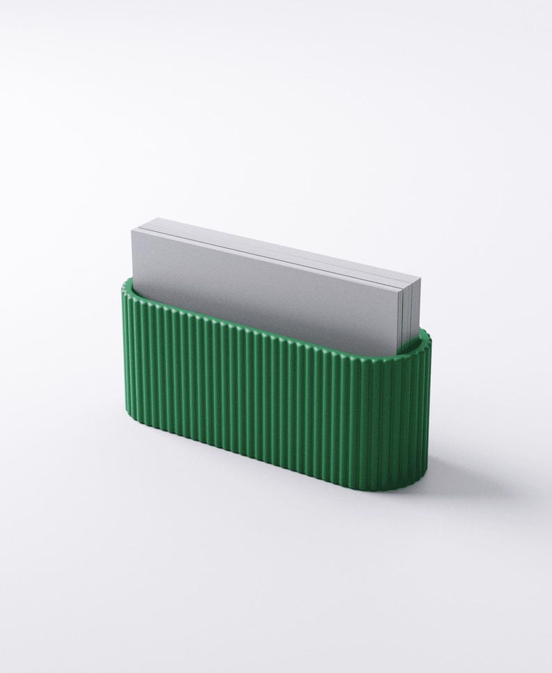 May include: A green, ribbed business card holder with a curved base. The holder contains a stack of gray business cards. The design is minimalist and modern, suitable for an office or desk setting.