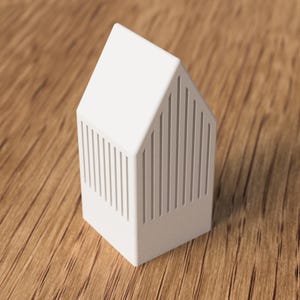 May include: A white, house-shaped decorative object with vertical lines on the sides. The object has a pitched roof and sits on a wooden surface. The design is minimalist and modern, suitable for home decor.