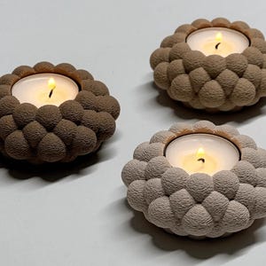 May include: Three decorative candle holders with lit candles. Each holder has a textured, bubble-like design in shades of brown and beige. The candles emit a warm, inviting glow, perfect for home decor.