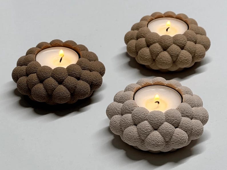 May include: Three decorative candle holders with lit candles. Each holder has a textured, bubble-like design in shades of brown and beige. The candles emit a warm, inviting glow, perfect for home decor.