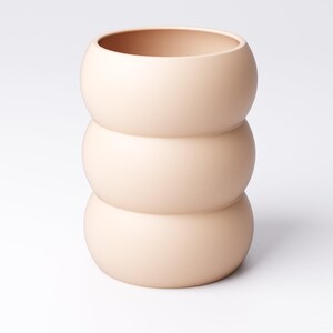 May include: A peach-colored ceramic vase with a unique stacked design. The vase is composed of three rounded sections, creating a bulbous shape. The top section has a wide opening. The smooth, matte finish gives it a modern aesthetic. Ideal for home decor.