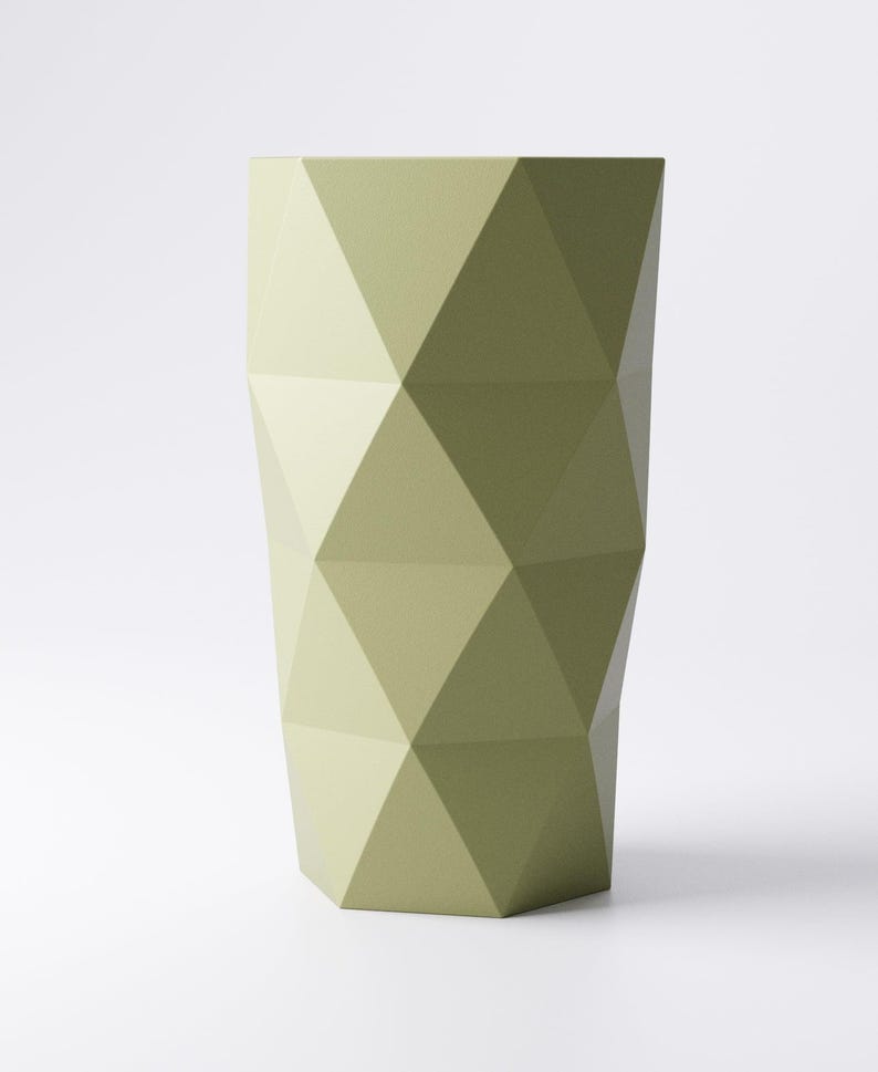 Op de afbeelding: Een hoge, geometrische vaas in een gedempte olijfgroene tint. De vaas heeft een facetontwerp, met talrijke driehoekige panelen die een gestructureerd oppervlak cre&euml;ren. De vaas staat tegen een effen witte achtergrond.