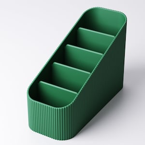 May include: A green desk organizer with four compartments. The organizer has a ribbed exterior and a slanted design. The compartments are separated by flat dividers. The overall shape is rectangular with rounded corners.
