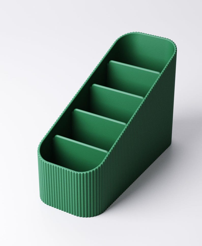 May include: A green desk organizer with four compartments. The organizer has a ribbed exterior and a slanted design. The compartments are separated by flat dividers. The overall shape is rectangular with rounded corners.