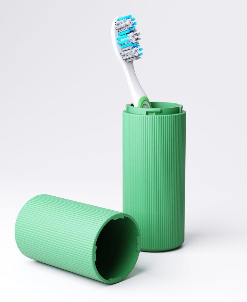 May include: A light green cylindrical toothbrush case with a ribbed texture. One half of the case stands upright containing a white toothbrush with blue and white bristles, while the other half of the case lies horizontally in the foreground.