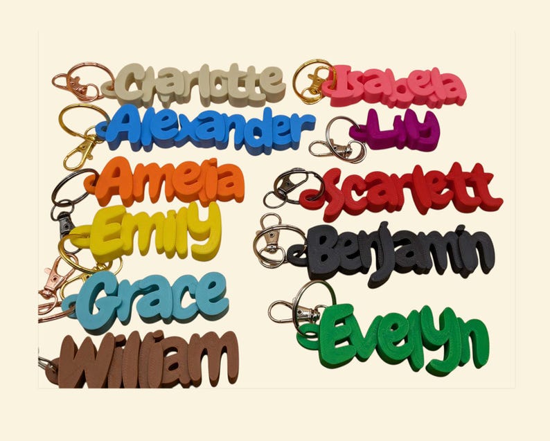 May include: A collection of colorful name keychains in various colors, including beige, blue, orange, yellow, teal, brown, pink, purple, red, black, and green. Each keychain features a different name in a bold, playful font, attached to a metal keyring.