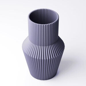Pu&ograve; includere: Un vaso color lavanda dal design geometrico. Il vaso ha un collo cilindrico e un corpo pi&ugrave; ampio e sfaccettato. Le creste verticali corrono lungo l'intera superficie, creando un aspetto strutturato. Il vaso &egrave; realizzato in un materiale solido e poggia su uno sfondo bianco.
