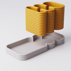 Puede incluir: Escultura abstracta moderna con base gris claro y bordes curvos apilados. Tres formas verticales amarillas en forma de U se elevan sobre la base. Dise&ntilde;o minimalista y contempor&aacute;neo.