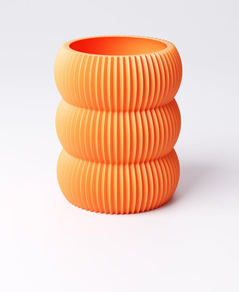 May include: An orange, three-tiered vase with a ribbed design. The vase has a cylindrical shape with rounded sections, and the vertical ribs create a textured surface. The bright orange color gives it a modern look.