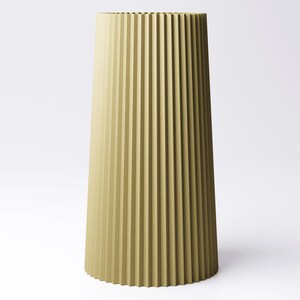 May include: A tall, olive-green vase with a fluted design. The vase has a wide base that tapers upwards to a narrower opening. The vertical grooves create a textured surface. The vase is set against a white background.