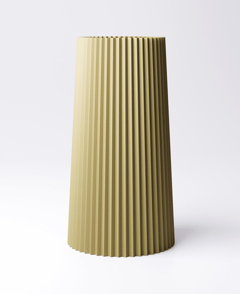 May include: A tall, olive-green vase with a fluted design. The vase has a wide base that tapers upwards to a narrower opening. The vertical grooves create a textured surface. The vase is set against a white background.