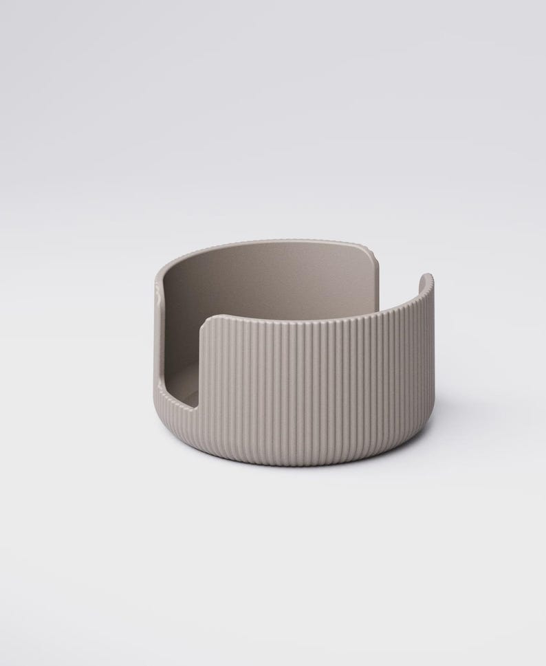 May include: A taupe-colored, semi-circular container with vertical ribbed detailing on the exterior. The open design features a curved back and a cutout on one side. The object is made of a solid material and sits on a white background.