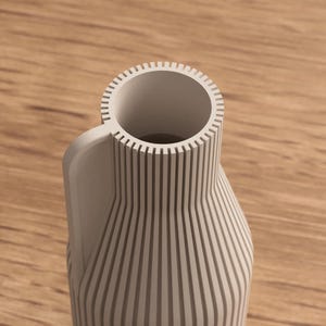 May include: A light gray vase with a handle and a cylindrical opening. The vase has vertical lines that run from the base to the top. The handle is curved and attached to the side of the vase. The vase is made of a solid material.
