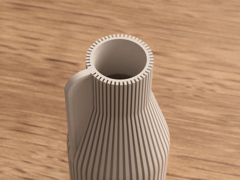 May include: A light gray vase with a handle and a cylindrical opening. The vase has vertical lines that run from the base to the top. The handle is curved and attached to the side of the vase. The vase is made of a solid material.